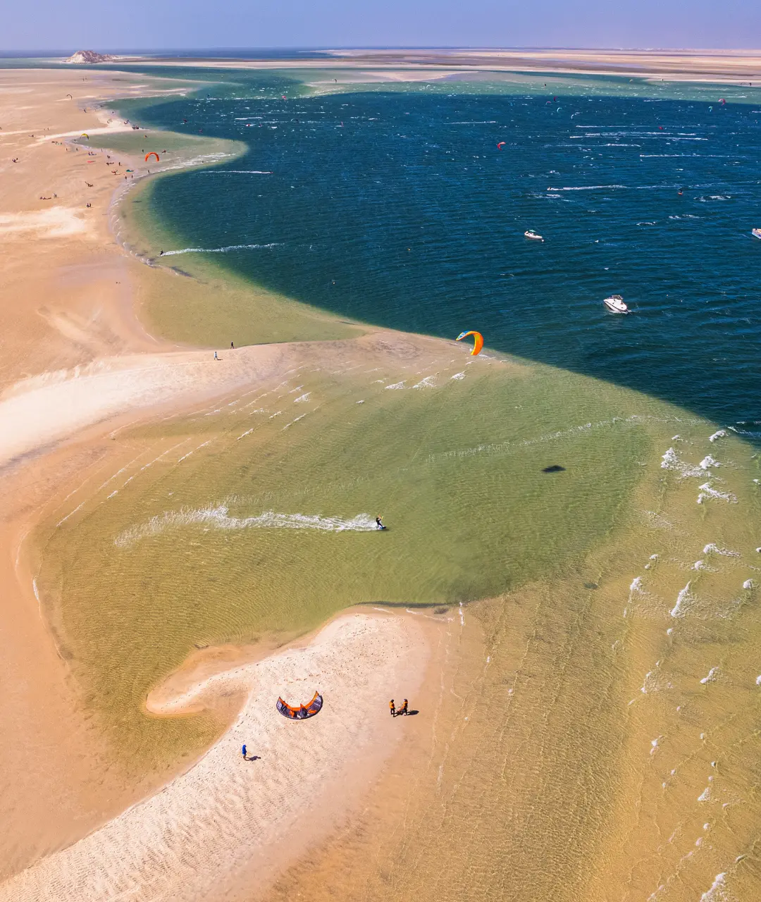 Aerial view of the turquoise Dakhla lagoon edged by dunes, with kitesurfers